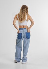 Light blue denim pants with darker blue patch pockets, side striped accents, and a relaxed fit. Worn with a white cropped top.