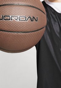 Basketboll med en texturerad yta i orange och svart, med "JORDAN"-logotypen framträdande. Bärs med en svart mesh-tröja.