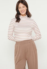 Maglietta a maniche lunghe a righe in rosa chiaro e bianco, con un collo alto. Abbinata a pantaloni beige a vestibilità ampia realizzati in tessuto morbido.