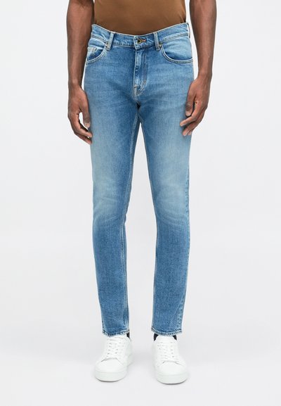 Jeans de mezclilla azul claro con un ajuste slim, diseño de cinco bolsillos, un desgaste sutil y costuras en contraste, combinados con zapatillas blancas.