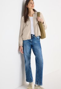 Sweat à capuche zippé beige clair avec capuche, poignets élastiques ; associé à un jean large bleu et des baskets beiges. Design simple, look décontracté.