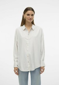 Camicia a righe con bottone in tessuto leggero. Presenta maniche lunghe, colletto e un orlo leggermente curvato. I colori includono bianco con righe pastello.