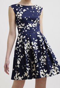 Marindräkt med vitt fjärilsmönster, korta ärmar, figursydd bodice och veckad kjol. Tillverkad av slät tyg med en strukturerad design.