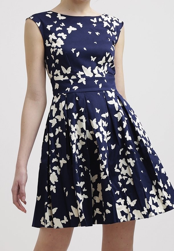 Marindräkt med vitt fjärilsmönster, korta ärmar, figursydd bodice och veckad kjol. Tillverkad av slät tyg med en strukturerad design.