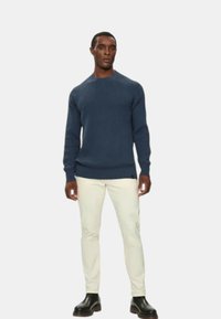 Maglione a coste blu navy con scollatura rotonda, abbinato a pantaloni color crema e stivali neri, che creano una silhouette aderente.