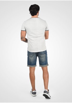 Szary T-shirt krótki rękaw z czarnymi wykończeniami, w połączeniu z niebieskimi szortami dżinsowymi podwiniętymi na brzegu, model pokazany z tyłu, nosi szare sneakersy.