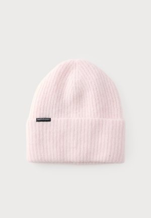 Bonnet en tricot côtelé rose pâle doux avec un revers plié et une petite étiquette noire sur le côté sur un fond clair uni.