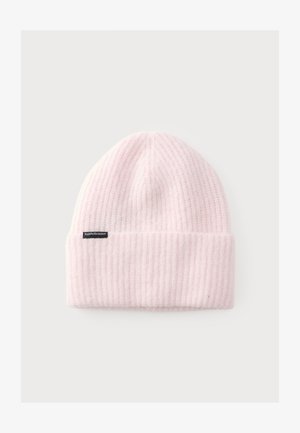 Bonnet en tricot côtelé rose pâle doux avec un revers plié et une petite étiquette noire sur le côté sur un fond clair uni.