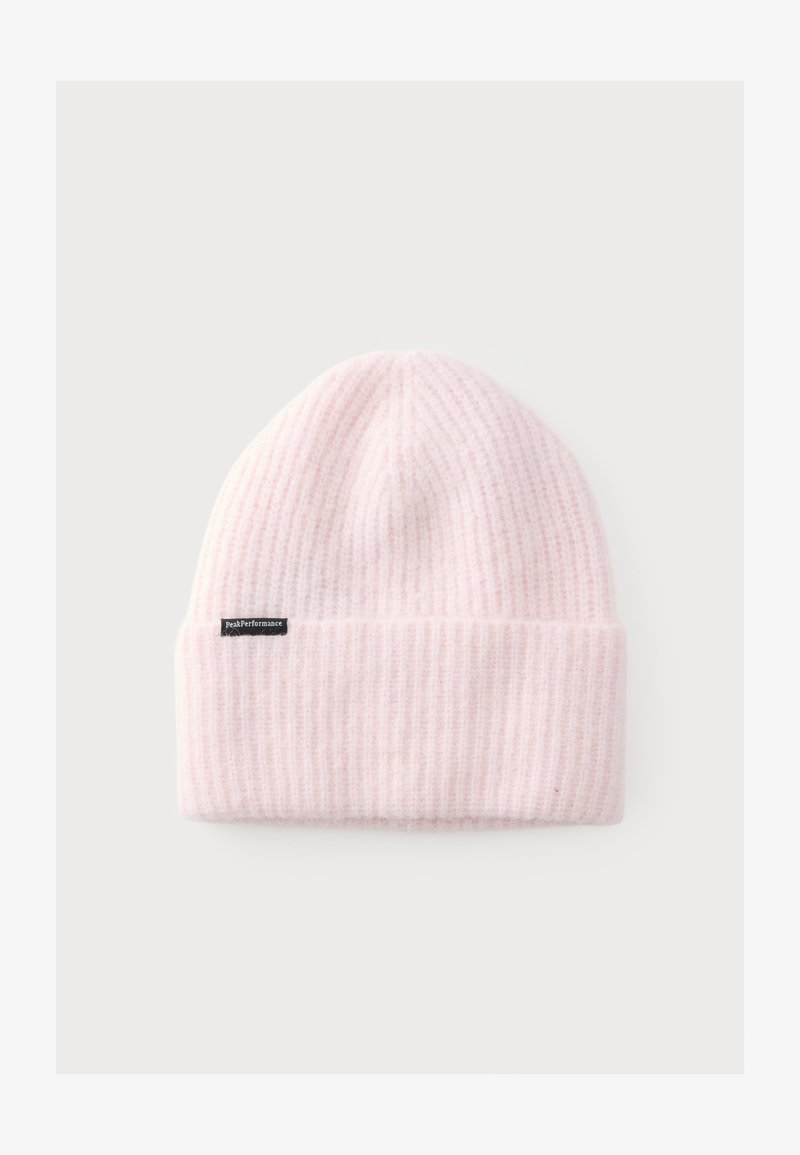 Bonnet en tricot côtelé rose pâle doux avec un revers plié et une petite étiquette noire sur le côté sur un fond clair uni.