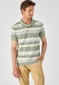 Groene gestreepte polo met gele en grijze horizontale strepen; heeft een korte kraag, een drieknoopsluiting en een borstzak.