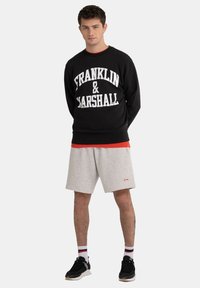 Black sweatshirt with "FRANKLIN & MARSHALL" in large white text, paired with gray athletic shorts and black sneakers, featuring red accents.