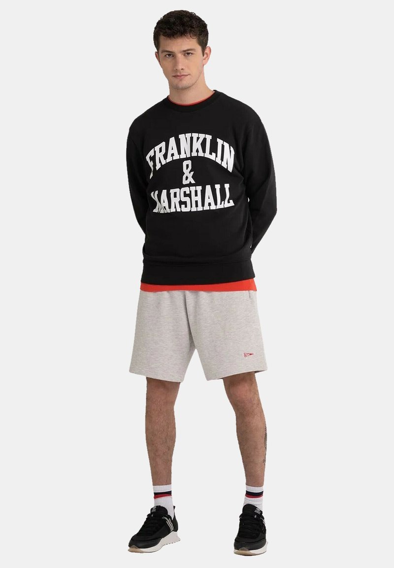 Black sweatshirt with "FRANKLIN & MARSHALL" in large white text, paired with gray athletic shorts and black sneakers, featuring red accents.