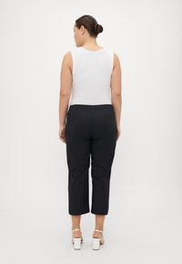 White sleeveless top with round neckline, paired with black cropped pants, featuring an elastic waistband. Model wearing white block heels.