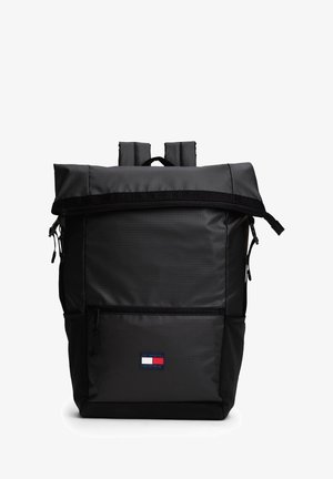 Sac à dos noir à rabat enroulable, fabriqué en tissu durable, doté d'une poche zippée à l'avant, de sangles réglables et d'un patch logo en bas.