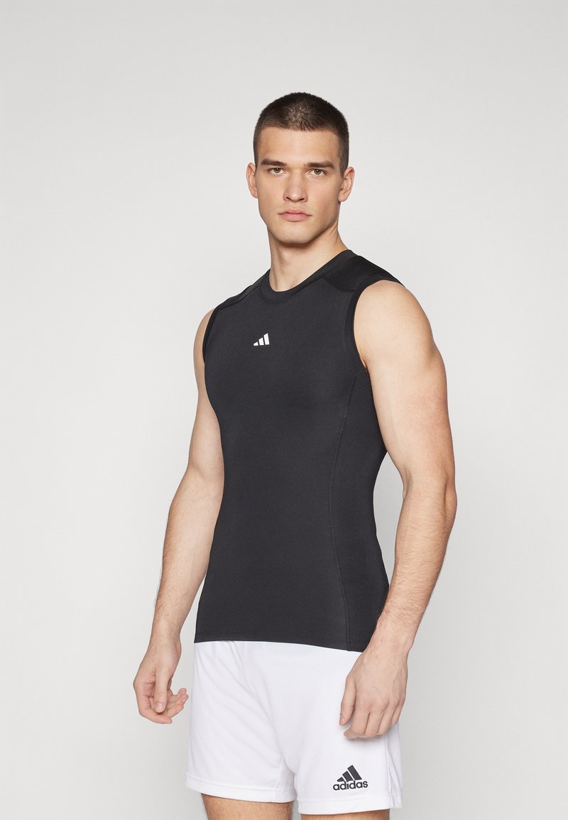 Black sleeveless athletic top with a fitted design and flat seams. Features a small white logo on the chest and a smooth, stretchy texture.