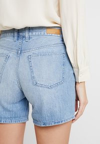 Shorts de mezclilla en azul claro con un acabado desgastado, que cuentan con una etiqueta de marca de cuero, dos bolsillos traseros y un corte clásico con dobladillos enrollados.