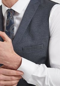 Ciemnoszara kamizelka w jodełkę zestawiona z białą koszulą, ozdobiona szczegółowym krawatem w wzór paisley oraz wykończoną kieszonką na kamizelce.