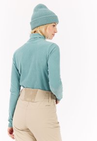Haut encolure montant côtelé bleu clair associé à un pantalon beige avec une taille texturée, vu de dos avec un bonnet tricoté assorti.