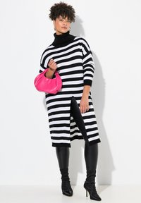 Abito a maglia a righe in bianco e nero, con collo alto, spacco laterale, abbinato a leggings neri e una borsa rosa. Stivali neri con tacco.