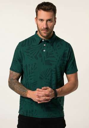 Camisa polo verde con un estampado de hojas, de manga corta y cuello de polo, con dos botones en el cuello. Textura suave, diseño informal.