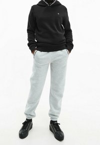 Felpa nera con un logo sul petto, abbinata a pantaloni della tuta grigi con accenti del logo sulle tasche e scarpe nere con lacci.