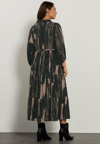 Maxi-Kleid mit einem schwarz-pinken abstrakten Muster, langen Ärmeln, einer taillierten Detail und einem gestuften Rock, kombiniert mit schwarzen Knöchelstiefeln.