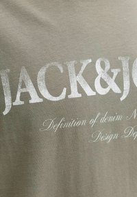 Λαδανί βαμβακερό μπλουζάκι με μεγάλα λευκά γράμματα "JACK&JO" και μικρότερα γράμματα "Definition of denim | Design Dep." Με έντονο, μοντέρνο στυλ γραμματοσειράς.
