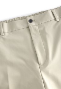 Pantalones beige con una textura suave, con cierre de botón y cintura elástica. Diseño simple con detalles en las costuras laterales.