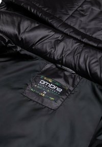 Chaqueta acolchada negra con una textura suave, presenta una etiqueta negra cosida en el interior que dice "esencia ombré" y tamaño "M".