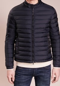 Námořnicky modrá péřová bunda s prošívanými panely, stojatým límcem, zipovým zapínáním, přiléhavými manžetami a lehkým žebrovaným lemem. Boční prvky z černé látky.