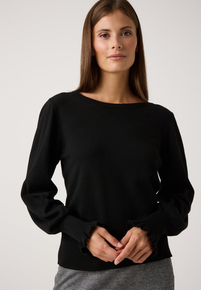 Pull en tricot noir à manches longues, avec des poignets à volants et un col rond. Texture douce et coupe ajustée.