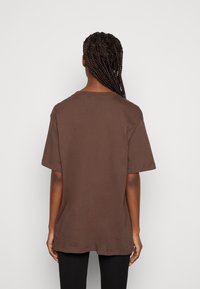 Hnědý bavlněný tričko s krátkými rukávy, volný střih, kulatý výstřih a rozparky na spodním lemu, zobrazeno ze zadní strany.