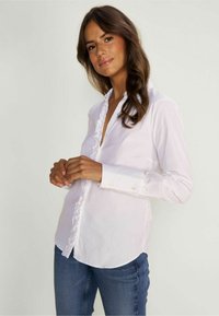 Witte button-up blouse met rimpelplacket, lange mouwen en knopenmanchetten, gecombineerd met blauwe spijkerbroek. Glad materiaal, casual pasvorm, afgeronde zoom.
