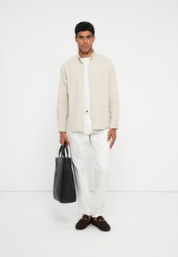 Beige vászon gombos ing, fehér póló, fehér nadrág, barna mokaszin, és egy fekete vászontáska. Egyszerű, modern design sokoldalú színekkel.