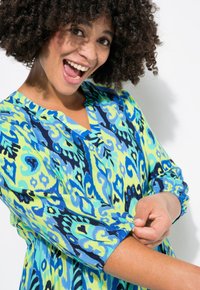 Vestido estampado colorido en azul, verde y amarillo con escote en V, mangas largas y puños fruncidos. Tejido suave y ligero con un diseño fluido.