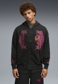 Czarna bluza z kapturem na zamek, z fioletowymi grafikami i napisami. Posiada kaptur i ściągacze na rękawach. Noszona z czarnymi szortami z kieszeniami i ozdobnymi detalami.