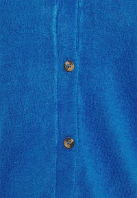 Blå stickad tyg med två bruna knappar fästa vertikalt längs mittsömmen.