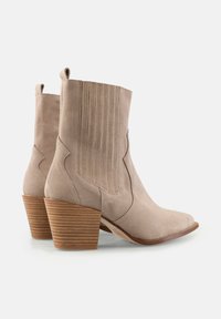 Cizme de gleznă din suede bej, cu vârf ascuțit, cusături laterale curbe, tab-uri laterale pentru tragere și un toc din lemn stratificat cu dungi orizontale.