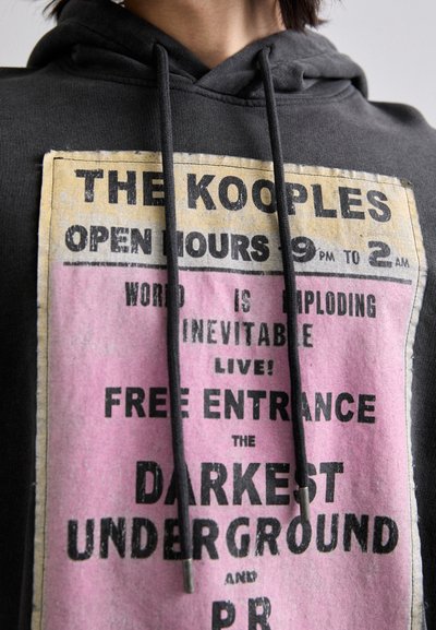 Czarna bluza z kapturem z dużym nadrukiem graficznym w kolorze żółtym i różowym. Tekst zawiera "THE KOOPLES" oraz "BEZPŁATNY WSTĘP", z sznurkami do regulacji i miękką teksturą.
