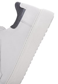 Zapatilla de cuero blanca con acento texturizado en gris, puntera redondeada, suela de goma y detalle de costura visible a lo largo del costado.