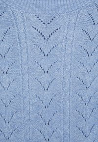 Svetle modrá pletenina s vzorem chevron krajky a vertikálními pruhy z kabelového pletení, ukazující texturu a detaily stehu.