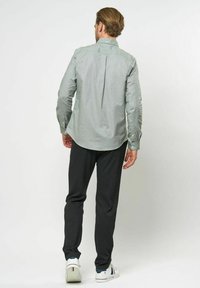 Ljusgrön skjorta med knäppning fram och en veck bak, ihop med mörkgrå byxor och vita sneakers. Slät tygkvalitet, avslappnad design.