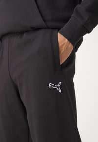Sorte sweatpants med en glat overflade, med elastisk talje og lommer. Bemærkelsesværdig hvid Puma-logo broderet på venstre side.