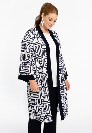 Kimono fluide blanc avec un motif abstrait bleu marine, bord noir sur les manches et les bords. Présente des manches larges et une coupe mi-longue.