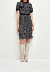 Abito a sheath in bianco e nero con texture, maniche corte, due tasche sul petto e vita aderente, abbinato a stivali beige al ginocchio.