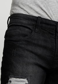 Musta farkut sisältävät kuluneen paikan, jossa on revitty reuna, tavalliset taskut ja suora malli. Texture näyttää sileältä, jossa on lievää kulumista.