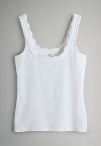 Biely tielkový top s rebrovanou textúrou, s ozdobnou čipkovanou lemovkou s vlnkovým vzorom okolo výstrihu a ramienok. Bez ďalších vzorov alebo ozdôb.