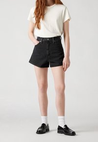 Black denim shorts with high waist, five pockets, and a raw hem. Paired with a white crew neck t-shirt and black loafers, accentuated by white socks.