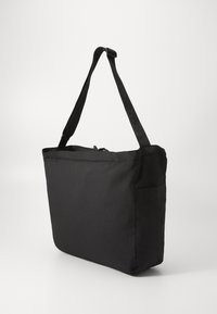 Svart totebag i rektangulær form, laget av slitesterk stoff. Har glidelås-feste og en utvendig lomme. Lang, justerbar stropp.