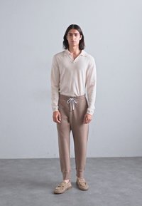 Svijetlosmeđi dugosleeve polo majica s kragnom i opuštenim krojem; uparen s mekanim, taupe tapered trenirkama i bež kliznim cipelama.